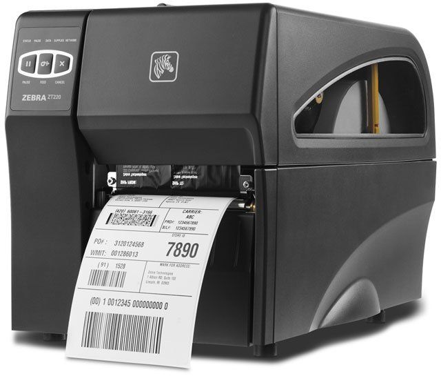 A Zebra ZT220 barcode label printer in black, with a label printing out from the bottom slot.